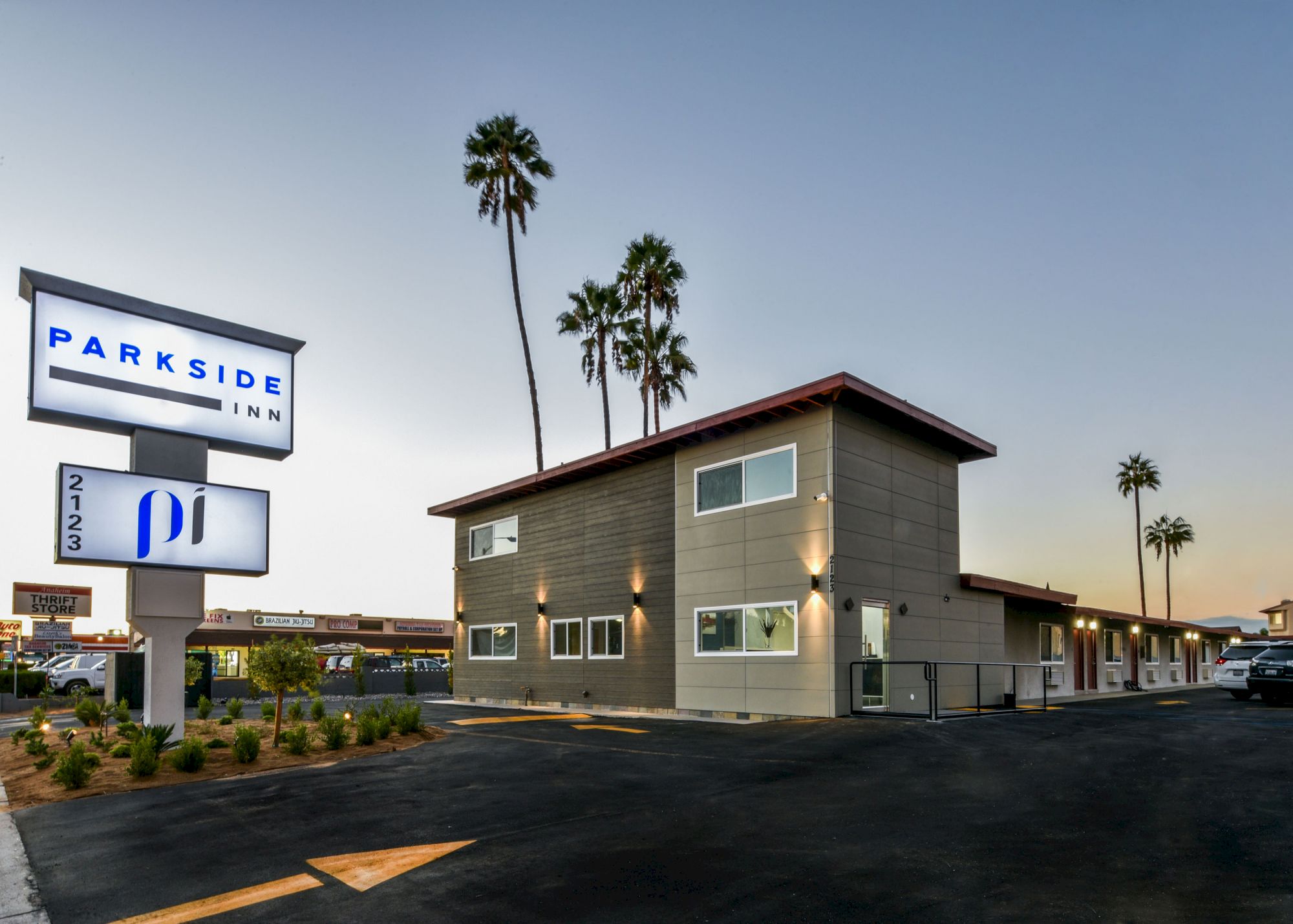 An exterior view of Parkside Inn with a visible sign, multiple rooms, and surrounding palm trees during twilight, asphalt paving in the foreground.